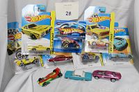 Photo of ten Hot Wheels cars including seven mint-on-card and three loose cars arranged on a white surface, showing carded packages and loose cars clearly.