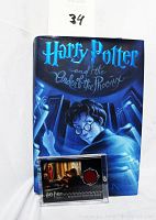 Photo showing the hardcover book with dust cover featuring Harry Potter artwork and the acrylic-encased costume card in front of it.