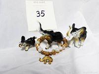 Three porcelain elephants with trunks raised in descending size order alongside a gold elephant charm and beaded bracelet