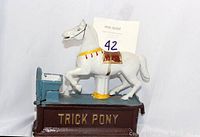 Front view of the vintage Trick Pony cast iron mechanical coin bank showing the white horse mounted on the brown base with 'TRICK PONY' lettering and the blue feed trough for coins.