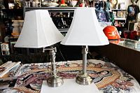 Pair of silver-tone metal lamps with white flared rectangular lampshades on a patterned table.