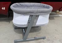 Side view of the bassinet showing grey tweed fabric and adjustable metal frame with mesh sides.