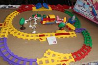 Colorful battery-operated train set arranged on circular multi-colored plastic tracks showing locomotive, animal passenger cars, trees, and traffic signs with the original box in background.