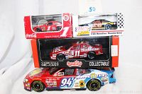 Five racing die-cast collectibles, four including one loose Bill Elliott #94 Ford Taurus blue and red with McDonald's logo, and three sealed mint in box models: Budweiser #11 Ford Thunderbird, Coca-Cola Monte Carlo #1 Chevrolet, and Havoline Thunderbird #28. Also includes vintage Miller American Racing pin.