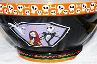 Close-up image showing the bowl's black exterior with an orange rim decorated with white skulls and bones, and a graphic of Jack Skellington and Sally framed in purple.