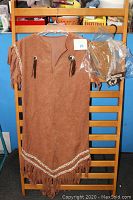 Brown faux suede dress with fringe sleeves and hem, decorated with braided trim and conchos with tassels, hanging on a rack