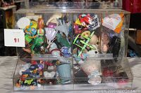 Front view of acrylic display case filled with assorted toys showing various characters and items inside compartments