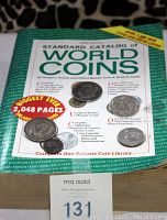 Front cover of 1985 Standard Catalog of World Coins showing book title and coin images, with coins placed on cover and MaxSold auction card.