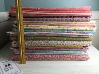 Stack of 26 lengths of floral cotton fabrics with ruler to show height approx 18 inches