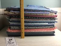 Stack of assorted cotton quilting fabric lengths showing approximate 9-inch height with ruler for scale