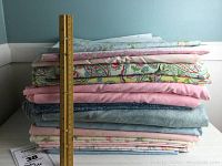 Stack of 12 fabric pieces, assorted pastel colors including pink, blue, and coordinated floral prints with 1 yard ruler placed vertically for scale.
