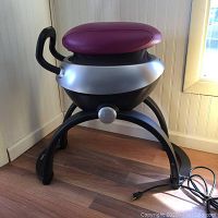 Side view of OSIM iGallop exercise machine showing maroon saddle seat, silver body, black legs, and power cord on wooden floor.