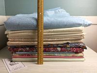 Stack of assorted quilting fabrics with ruler for scale, showing varied colors and patterns with a tall stack about 11 inches high