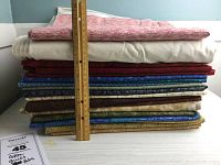 Stack of folded quilting cotton fabric lengths stacked with a ruler to show height, showing various colors and patterns