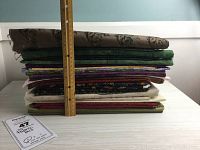 Stack of 11 assorted pieces of cotton quilt fabric showing thickness and size with a ruler for scale