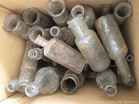 Top view of box with multiple old glass bottles showing variety of sizes and shapes, dirt-covered and dusty from excavation