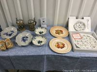 Photo of entire lot on table showing various plates, figurines, beer steins, trivet, and bowls