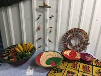 Photo showing an assortment of handmade Kenyan baskets of various sizes and colors filled with wooden carved fruits, a yellow batik cloth with African animal silhouettes, and a circular wreath decorated with small carved figures.