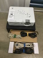 Top view of Sharp Notevision PG A10X projector on black box with box underneath holding multiple cords including power and VGA cables.