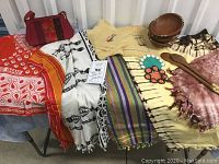 Photo showing five colorful handmade fabric pieces including tie-dye and printed textiles, a fabric handbag, and wooden bowls and spoons arranged on top.