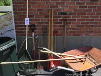 Wide view of yard tools set including wheelbarrow, rake, hand rake, shovel and pole digger leaning against wall