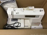 Embroidery machine in cardboard box with black power cord
