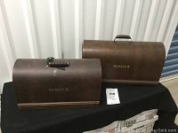 Two wooden domed-top Singer branded sewing machine covers side by side on a black surface.