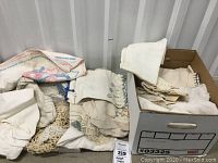 Box with assorted antique linens, embroidered pieces, chenille, tablecloths, and napkins appearing in need of TLC