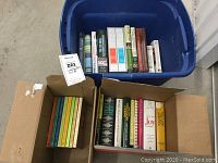 Cookbooks packed in blue plastic bin and two open cardboard boxes showing variety and number of titles.