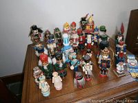 Photo showing 26 assorted nutcracker figurines in various colors and designs, placed on a wood table, showcasing their size, style, and minor wear.