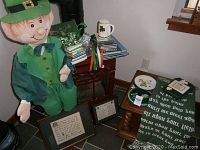 Photo showing a 48 inch leprechaun statue dressed in green, framed pictures, Irish books, CDs, and other Irish decor on floor and small tables