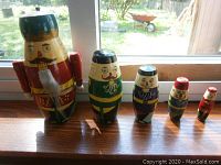 Photo showing a set of five wooden nesting nutcrackers arranged in descending size order on a window sill.