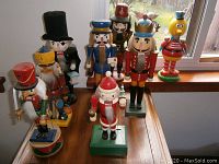 Photo of nine wooden nutcrackers including varied characters such as Santa Claus, soldier, pirate, reindeer, and bird, arranged on a wooden surface in front of a window.