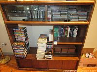 Full view of the wooden TV cabinet with DVDs, VHS tapes, and CDs visibly stored on shelves.