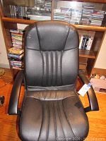 Front view of black office chair showing padded backrest with vertical stitching and padded armrests.