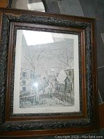 Framed black and white village street scene with trees and buildings, ornate carved dark wood frame