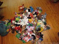 Pile of assorted plush toys on wooden floor, including Beanie Babies, Teenie Beanies, Disney and Veggie Friends characters visible