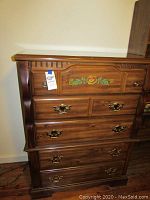 Front view of Basset 5 drawer dresser showing wood finish, brass handles, and floral detail on top drawer.