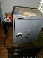 Side view of a vintage gray metal safe with a combination dial lock and some rust spots, showing the closed door.