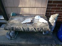 Front and side view of resin outdoor bench showing faux wood grain top, two white wings, face decoration, and gnome figure support on right end.