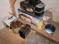 Wide view of cooking items on wooden shelf including large crock pot, toaster, boxes for other appliances and various kitchen accessories.