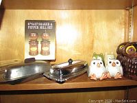 Close-up of metal butter dish with lid, ceramic owl salt and pepper shakers in white and green on wooden shelf.