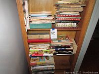 Multiple bookshelves filled with stacked cookbooks including visible titles Cookie Cookery and Wear-Ever New Method Cooking.