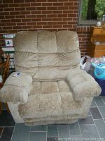 Full front view of beige upholstered reclining chair with visible wear on the seating area and armrests.