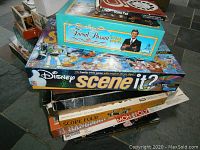 Stack of board games including Trivial Pursuit Game Show, Disney Scene It 2, Monopoly, Hangman and more.