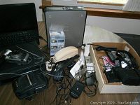 Photo showing various devices on a table including desktop computer tower, laptop, camera, and phone with cables