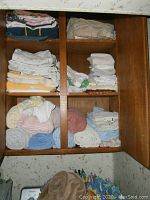 Wood shelving with stacks of folded towels and sheets in white, beige, pink, blue, and patterns.
