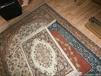 Photo showing three area rugs layered: small cream rug with medallion on top, medium floral patterned rug in the middle, large darker floral patterned rug at bottom