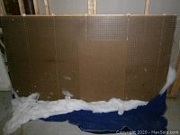 Large brown pegboard over 10 feet wide shown upright with white and blue fabric beneath it, with visible wear marks and scuffs on surface.