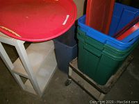 White two-shelf plastic shelving unit with red lids placed on top, showing side angle with blue and green storage totes in background.